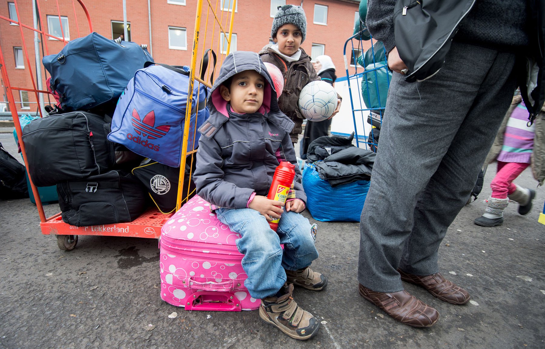 Zwischen Gepäckstücken und Erwachsenen warten zwei Flüchtlingskinder in der Hessischen Erstaufnahmeeinrichtung (HEAE) in Gießen (Hessen) auf ihre Registrierung. Foto: Boris Roessler/dpa