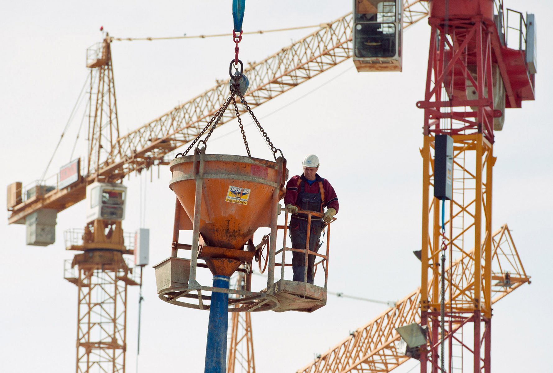 Vor Baukränen wird ein Bauarbeiter am 17.03.2012 auf einer Baustelle in Frankfurt am Main mit seiner Betonpumpe von einem Kran in die Höhe gezogen. Foto:  Boris Roessler/dpa 