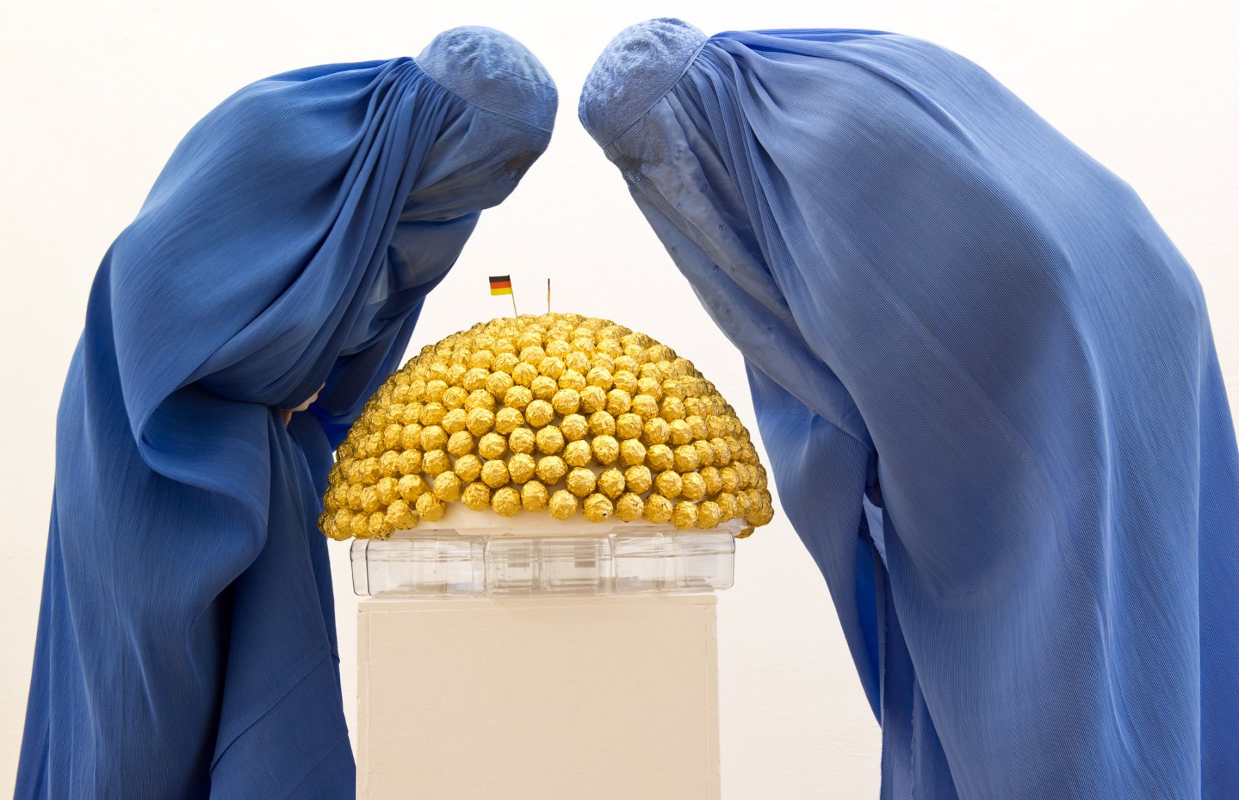 Eine Burka tragen Besucherinnen der Ausstellung "Burquoi" im Kunstverein in Wiesbaden. Dabei beugen sie sich über eine Halbkugel mit Schokoladenpralinen. Foto: Boris Roessler/dpa  