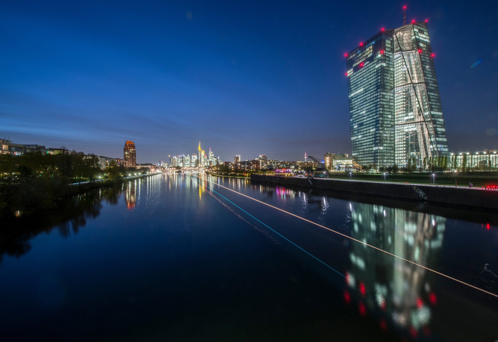 Im letzten Licht des Tages spiegelt sich die Zentrale der Europäischen Zentralbank (EZB) am 01.11.2017 im Wasser des Main, während die Bordlichter eines vorbeifahrenden Schiffes farbige Leuchtspuren durch die Dunkelheit ziehen. 