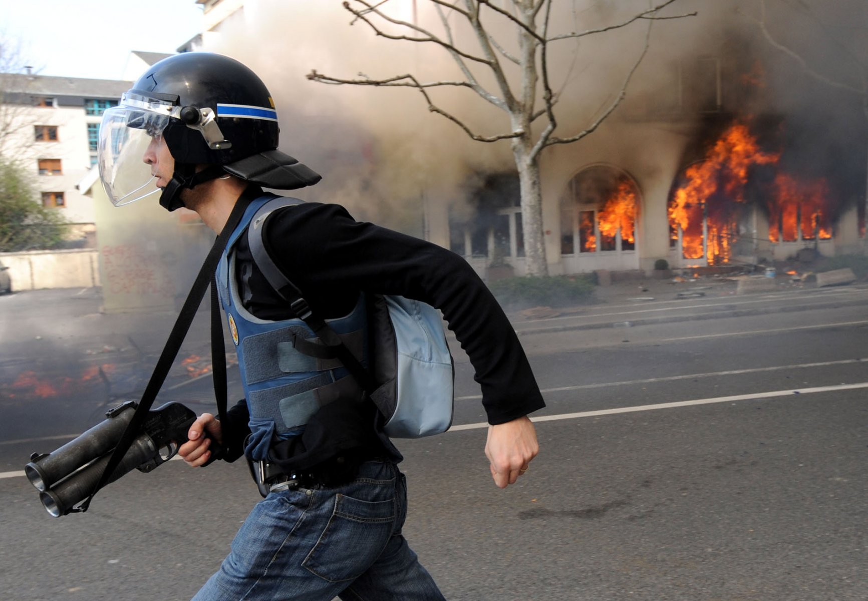 Mit gezogener Waffe läuft dieser Beamte einer Spezialeinheit am brennenden Ibis-Hotel in Straßburg vorbei, nachdem dieses am Samstag (04.04.2009) von Autonomen in Brand gesteckt wurde. Militante NATO-Gegner haben Brandsätze in das Hotel und mehrere andere Gebäude geworfen.  Foto: Boris Roessler    +++(c) dpa - Bildfunk+++