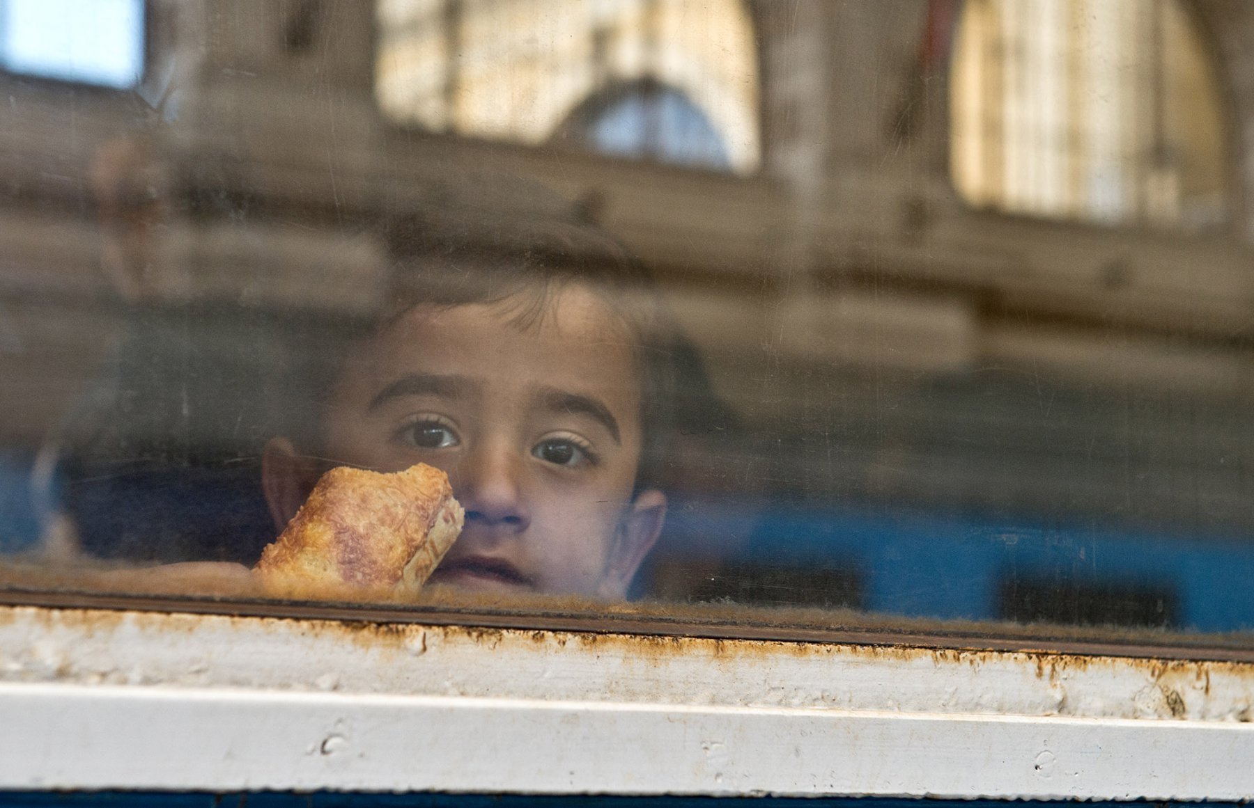 Mit einem Stück Brot in der Hand blickt ein kleiner Junge am 06.09.2015 bei der Abfahrt eines Zuges in Richtung Österreich am Ostbahnhof in Budapest, Ungarn aus dem Fenster. Foto: Boris Roessler/dpa